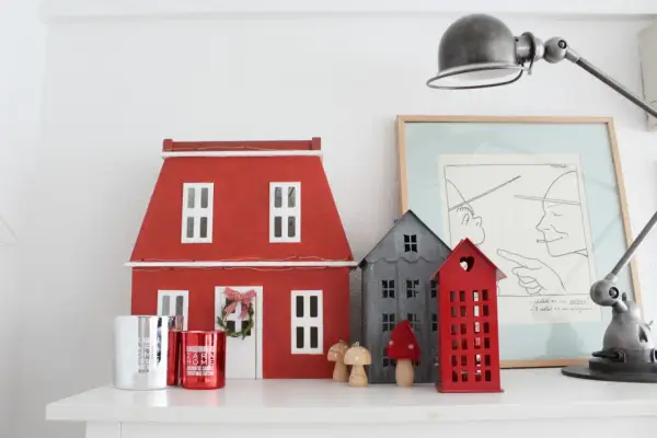 Un pueblo de casitas de navidad de madera, con una casa roja grande y otras más pequeñas, adornos y velas.